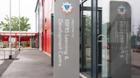 RBFRS The entrance to the new training centre. There's a glass door on the right hand side, and a sign with the fire service logo on it saying "Welcome to RBFRS Learning & Development Centre".