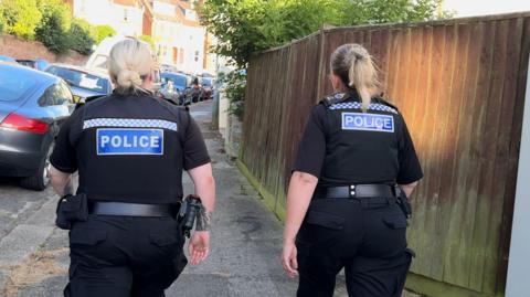 Two Sussex police officers walk down a residential street in Hastings