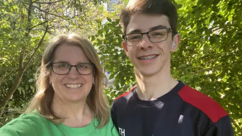 Family handout A teenager with glasses and his mother stand in a garden on a sunny day.