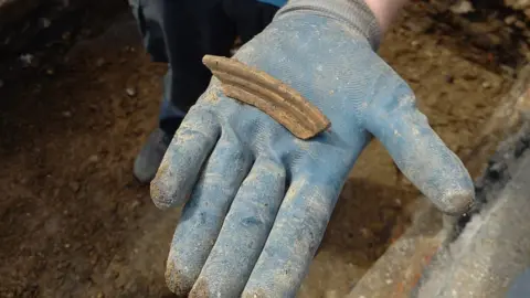St Albans Museums A gloved hand covered in dirt is holding a fragment of pottery