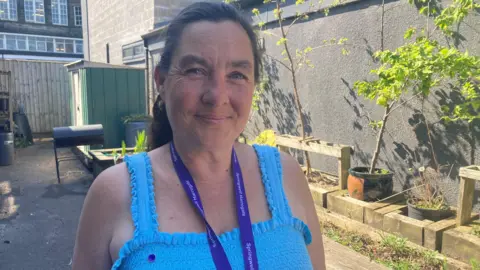 BBC/Emma Glasbey A middle-aged woman in a blue vest wearing a lanyard