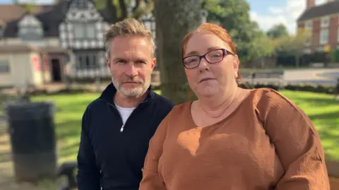 Two residents from Albrighton sat on a bench, posing for a photo. The man on the left is wearing a black jumper, while the woman on the right is wearing glasses and a brown top.