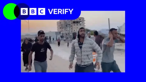 Gazans running after the Israeli strike on Khan Younis. Three men can be seen in the image. One man is wearing a grey jacket, the others are wearing t-shirts. A damaged building can be seen in the image. 