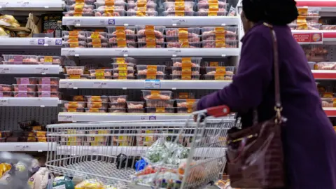 EPA Woman wearing a purple coat wheels a trolley at the refrigerated section of a supermarket.