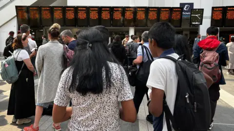 A crowd stands in front of a row of screens that should show train departure times but all say "Special Notice" on them.
