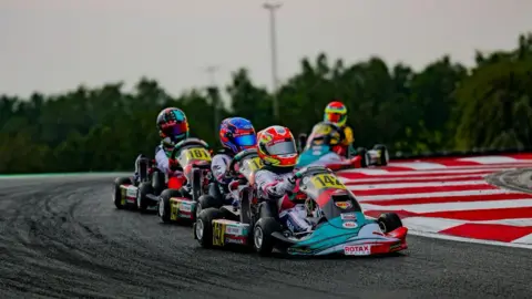 Images of karting competitors navigating a bend on a track. There are red and white chevrons to the side and trees in the background.