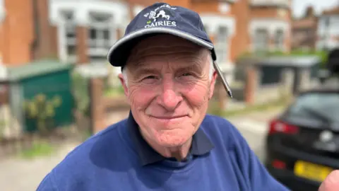 Man in Parker dairies hat with cow and pen over ear smiles 