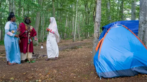 Three feet of feet, dressed in knitted jumper and robbers and jewelry and jewelry, standing beside the blue tents in the forest.