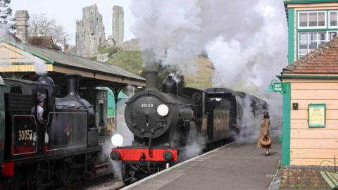The black T9 steam locomotive at Corfe Castle station with the castle ruins on the hill in the background