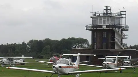 Anthony Parkes/Geograph Small aircraft in front of the control tower at Barton Aerodrome in Eccles.