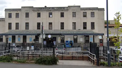 A train station with black iron gates fronting a beige rectangular building 