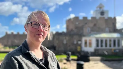 Abbi Saunders wearing glasses with blond hair swept across her face with the Clock Tower cafe in a blurred background