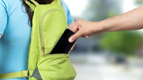 Close up of a thief hand stealing a phone from a tourist woman's bag on the street