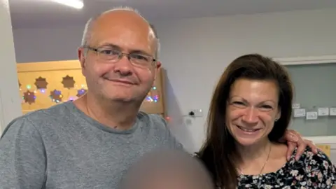Family handout Maxie Allen (right) and his partner Rosalind Levine smile while posing for a photo and looking directly at the camera standing in what looks like some kind of locker room.