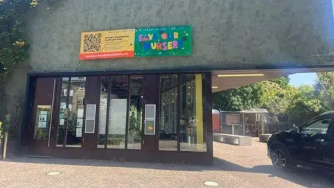 Exterior of a nursery building with banners reading “Save Our Nursery” displayed above the entrance.