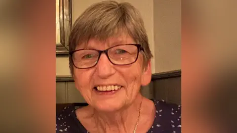 Image of Elizabeth, who has short brown hair. She is wearing glasses and has a gold necklace on.