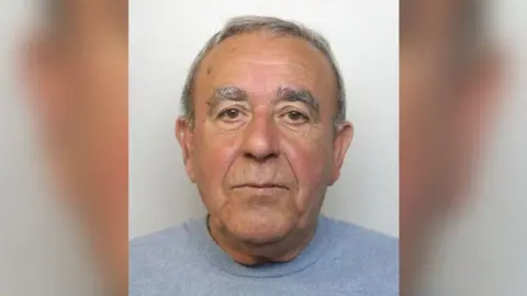 Custody image of Peter Lazarides - an man in his 70s, wearing a grey jumper. He has grey hair.