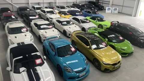 National Vehicle Crime Intelligence Service A view from a high vantage point of 25 high-value cars inside a warehouse