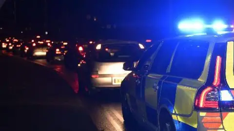 A queue of traffic on a road, all with their red break lights on and a police car which has its blue lights on at the back