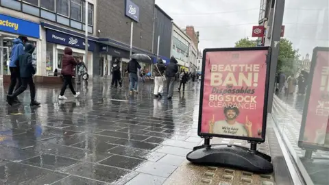 A sign for disposable vape sale on a damp Leicester street