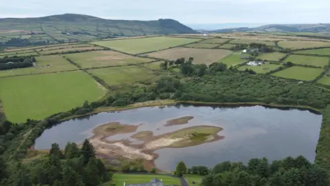 An arial view of the reservoir, you can see fields around and hills in the background.