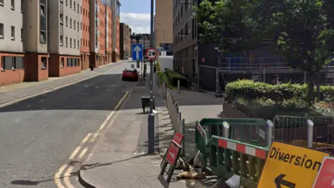 Google Residential street with student blocks on one side. There are a number of road signs, including one indicating a diversion. 