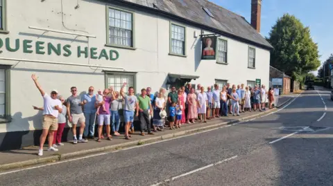 GORDON RIDGEWELL A group of over 30 people stand in front of a white pub with the Queens Head lettering and sign hanging above them