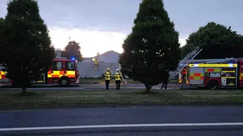 RTÉ red and yellow fire trucks and firefighters looking onto a smokey site