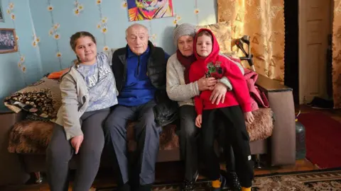 Family handout Oleksandra (left) and Kyrylo (right) sit on a sofa with their grandparents in Ukraine. 