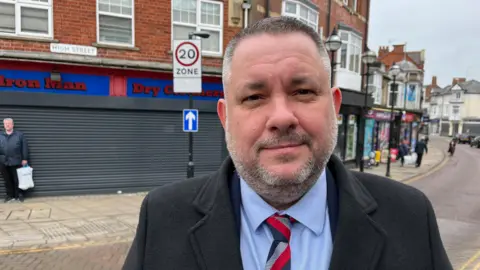 Jason Smithers standing in the street with a striped tie and a black coat