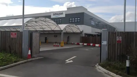 A grey building in the distance with the 'amazon' sign. The gates to the compound is open.