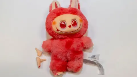 Fake Labubu toy, bright/pink colour, with bits fallen off.