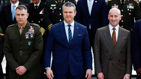US Secretary of Defence Pete Hegseth standing in a blue suit and tie.