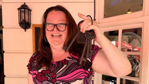 A woman smiles holding some large keys. 