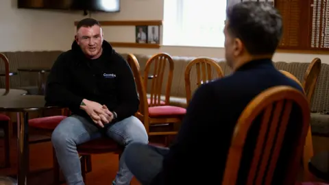 Ross is sitting in the rugby club, opposite the interviewer 