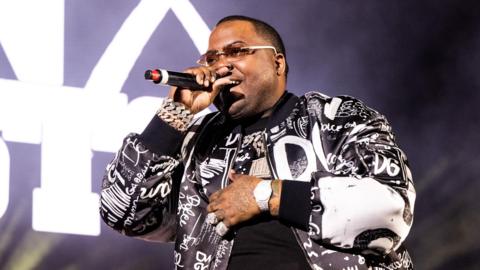 Sean Kingston wears a black and white jacket and sings into a microphone