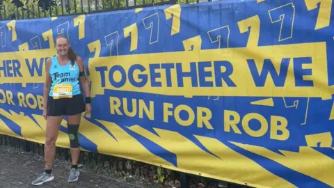 A woman standing in front of a Leeds Marathon banner. The colours are blue and yellow