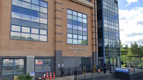 The outside of the community diagnostic centre in Telford. It is light brown and dark grey brick with many windows and a glass door. There is silver lettering on the wall that says "Hollinswood House"