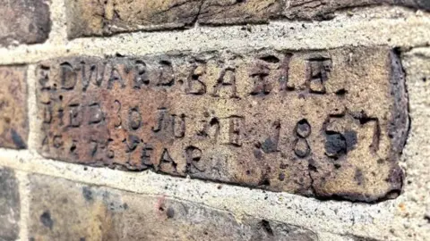 West Hertfordshire Teaching Hospitals NHS Trust A close up of a brick with engravings. It commemorates a former resident who died at the workhouse aged 76, in 1857.