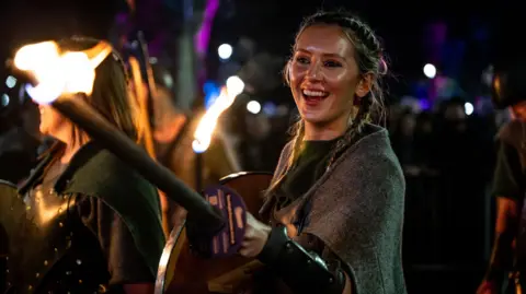 Ian Georgeson A woman carrying a flaming torch and a shield during the torchlight procession in Edinburgh