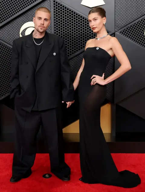 Getty Images Justin y Hailey Bieber visten trajes negros con collares plateados mientras posan para fotos en la alfombra roja de los Premios Grammy.