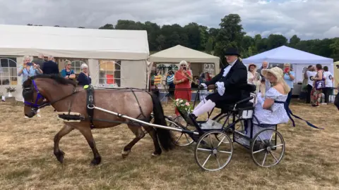 Horse pulling cart with man driving and woman in regency dress sat in the buggy.