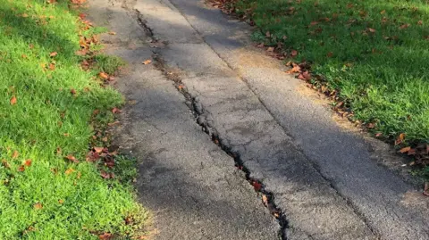 A thin section of pavement with a large crack running along the full length of it