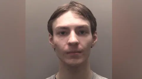 A police custody photograph of Darren Rigby who has brown hair and is wearing a grey jumper over a black t-shirt
