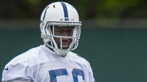 He is wearing his American football uniform, but the image is cut just below his shoulders. He is wearing a white helmet with a blue stripe down the middle and a white tshirt with blue detailing