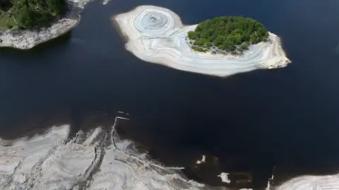 An aerial view of Haweswater reservoir, which shows receding water levels exposing light brown silt-beds.