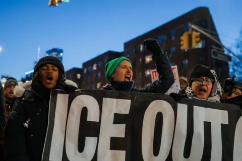 People in New York City carry a banner that reads "ICE OUT".