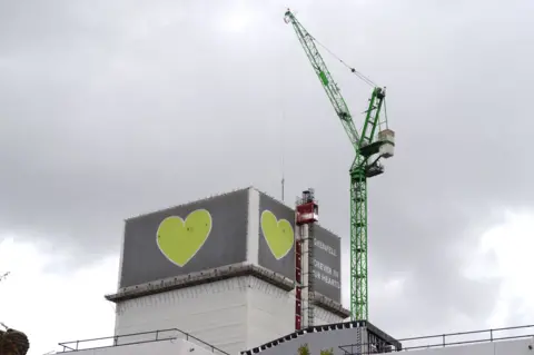 PA Media A crane is seen over the Grenfell Tower in west London where a large green heart is still visible on the top floors of the tower block