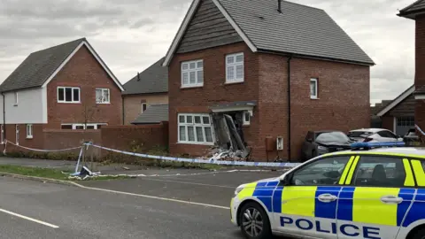 Sam Read/BBC A police car outside the damaged property which has police tape in front of it