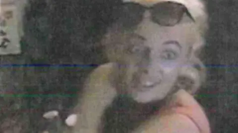 Merseyside Police A blurry CCTV still showing a woman with blonde hair and a pink vest-top, with sunglasses perched on her head.